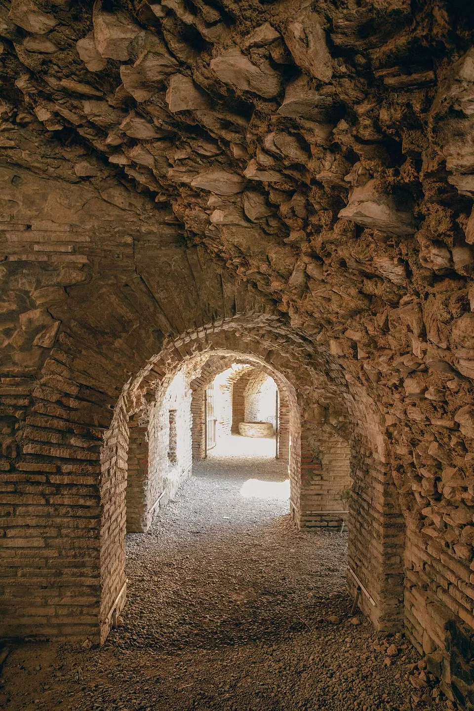 A long vaulted corridor of stone and brick with a sequence of arches leading into light.